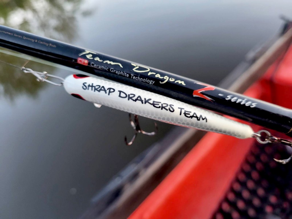 Wobler z ręcznym napisem Shrap-Drakers Team przy wędzisku, na łodzi